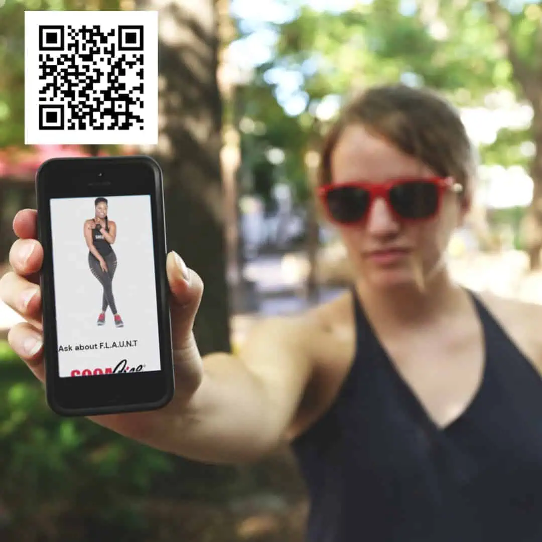 A woman holding up a phone with a digital business card displayed as a QR code on it.