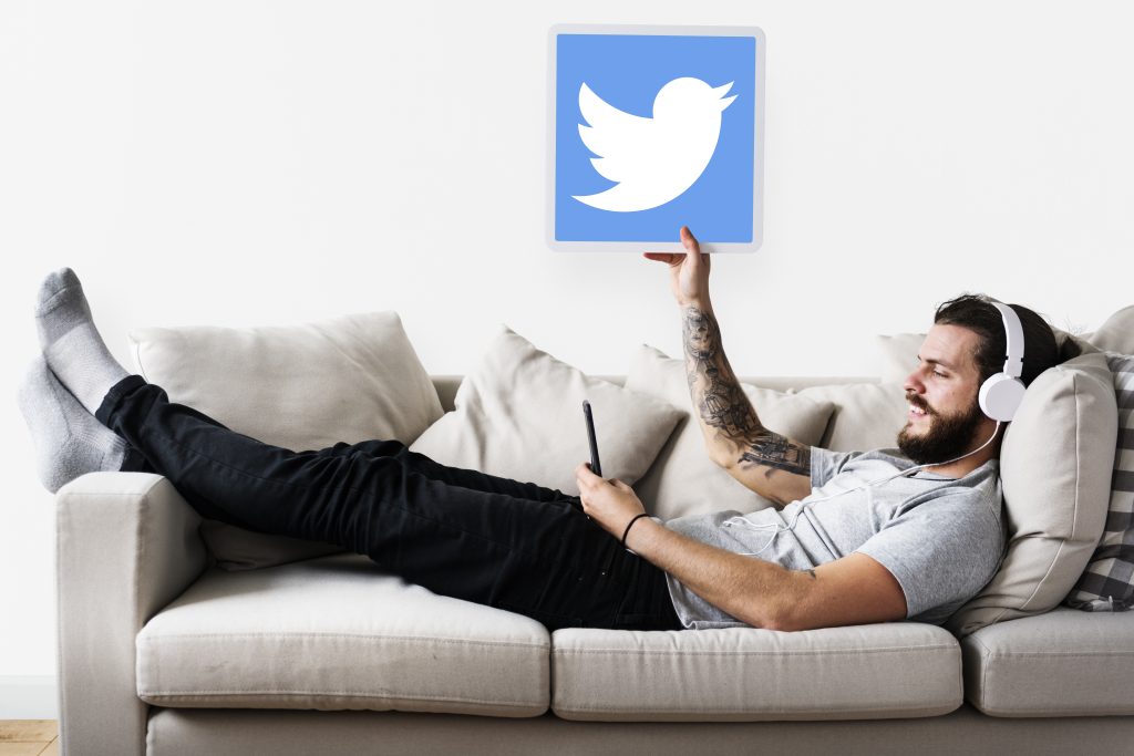 Social Media And Business: Choose The Right Platform For Your Business A man relaxes on a couch, headphones on, tablet in hand showcasing the Twitter logo—pondering how to pick the best social media platform for his needs, how to pick the best social media platform